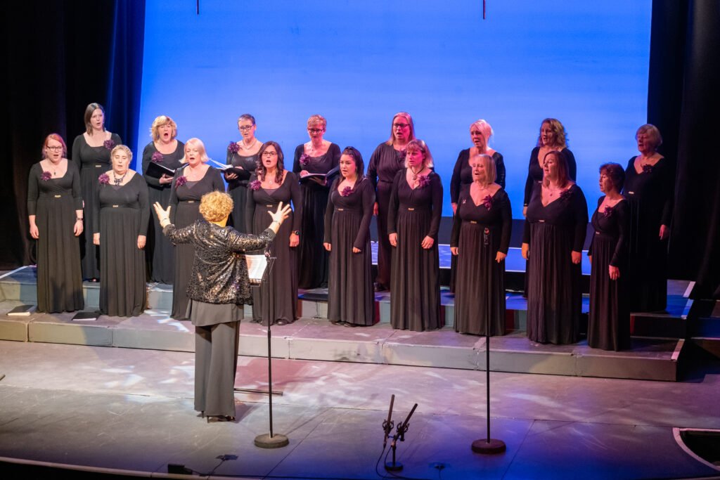 Jessa conducting the York Military Wives Choir, all dressed in black evening wear, at the Joseph Rowntree Theatre York